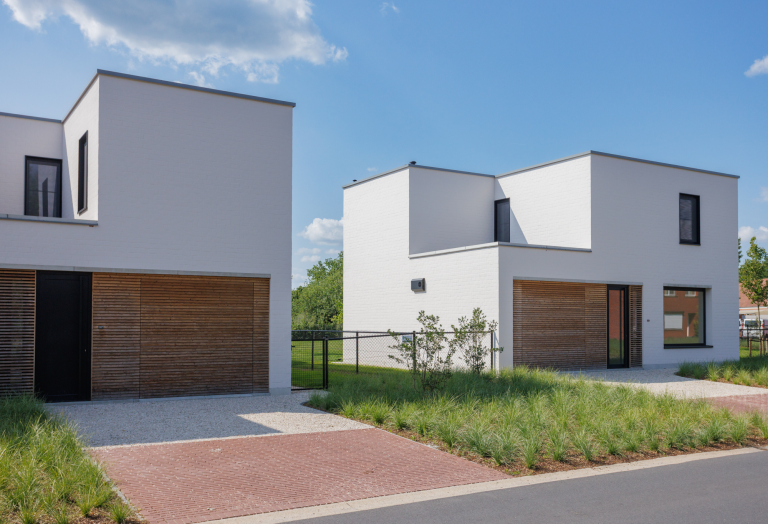 De voortuinen van moderne villa's. Je ziet groene grassen en een oprit gemaakt van lichte kiezels en rode klinkers.